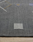 Sleek Inviting Gray Flatweave Rug lies partially unfurled on a light wood floor, revealing a portion of its subtle gray texture and inviting flatweave construction in a bright, airy setting.