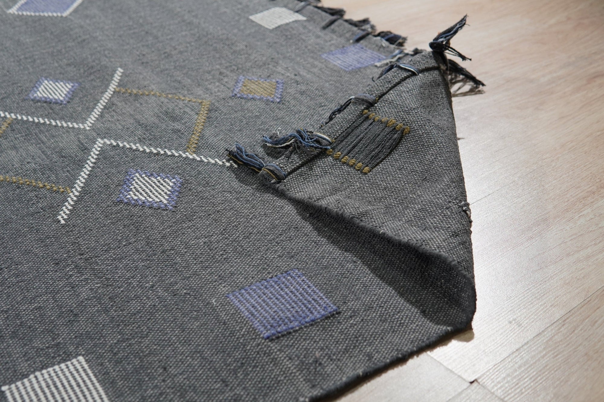 Sleek Inviting Gray Flatweave Rug layered over light hardwood flooring in a bright, modern living room; texture and subtle pattern are visible in the gray flatweave.