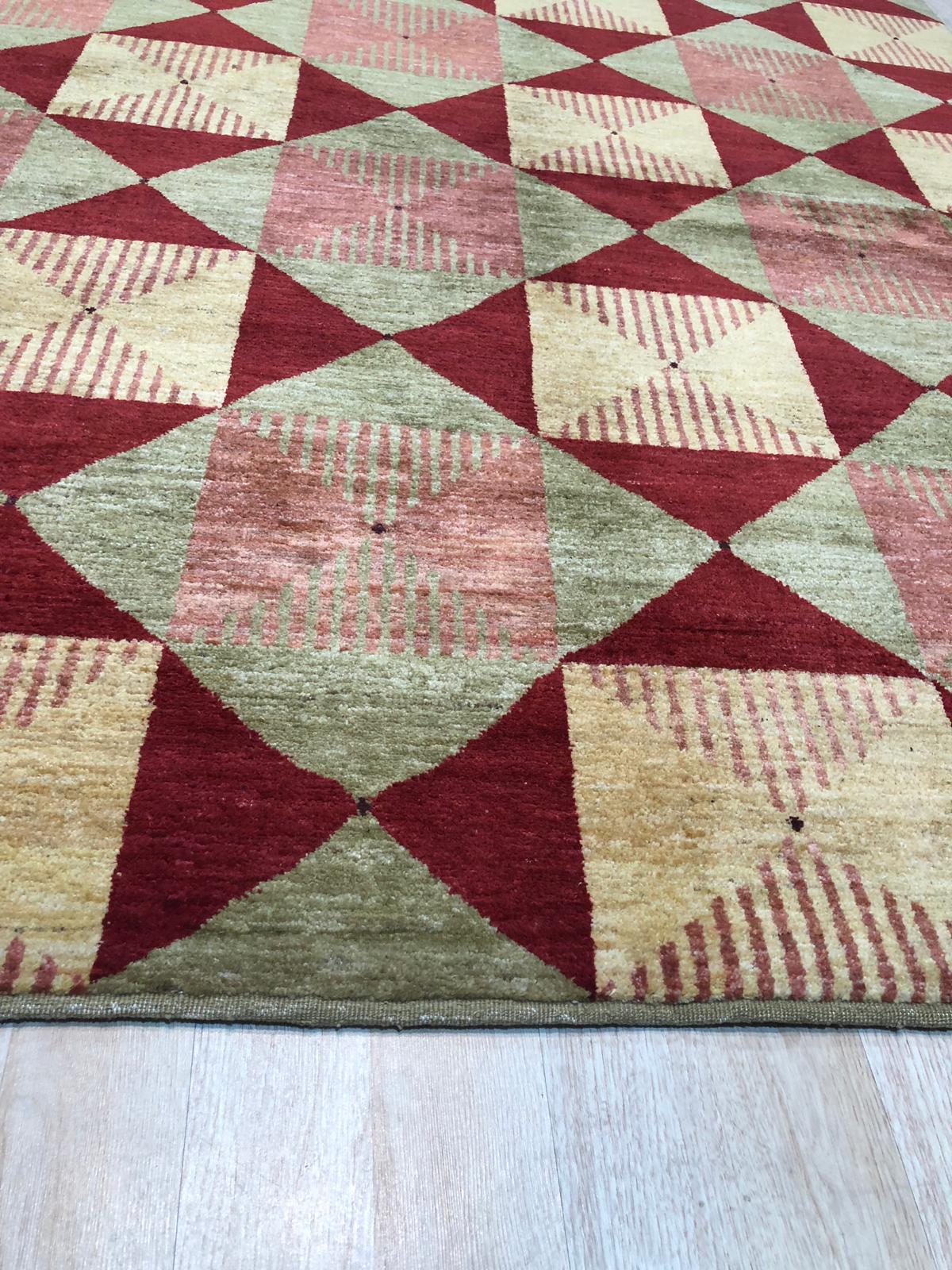 Sloane Diamond Red Hand Knotted Afghan Wool Rug, showcasing intricate diamond patterns woven in rich red Afghan wool, graces a softly lit interior.