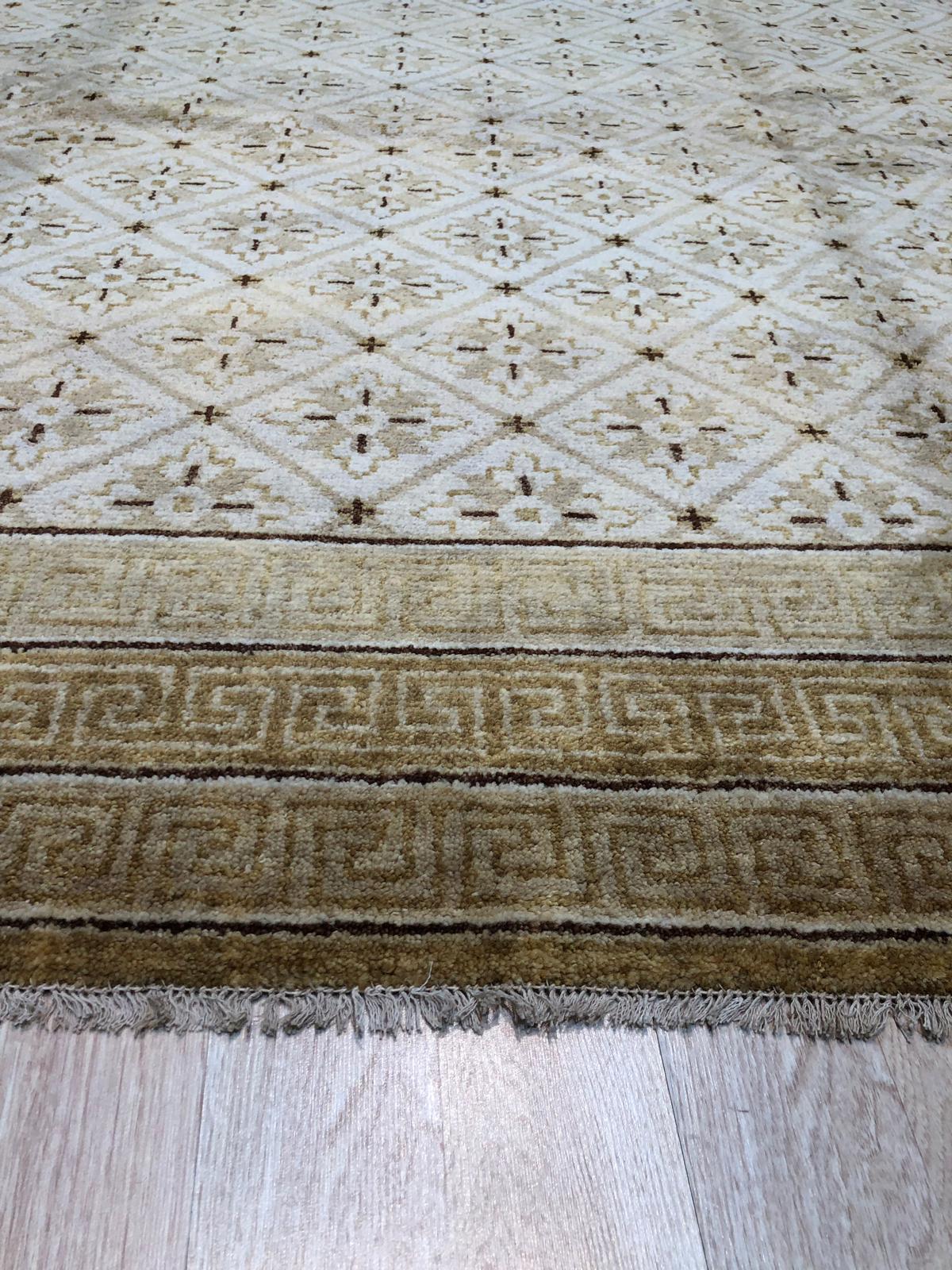 Trendy Handcrafted Beige Hand Knotted Wool Rug lies elegantly on a polished hardwood floor, its subtle beige hues and hand-knotted texture creating a warm and inviting atmosphere in a minimalist living space.