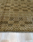 Rhea Majestic Brown Hand Knotted Wool Rug, its warm brown tones and hand-knotted texture grounding a living room scene with a neutral sofa and hardwood floors, showcasing its scale and integration into a modern interior.