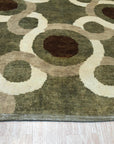 Talia Artistic Green Hand Knotted Wool Rug graces a living room, its verdant hues and artistic patterns grounding the space beneath a sleek, modern sofa. Soft wool texture and hand-knotted construction add depth to the room's sophisticated design.