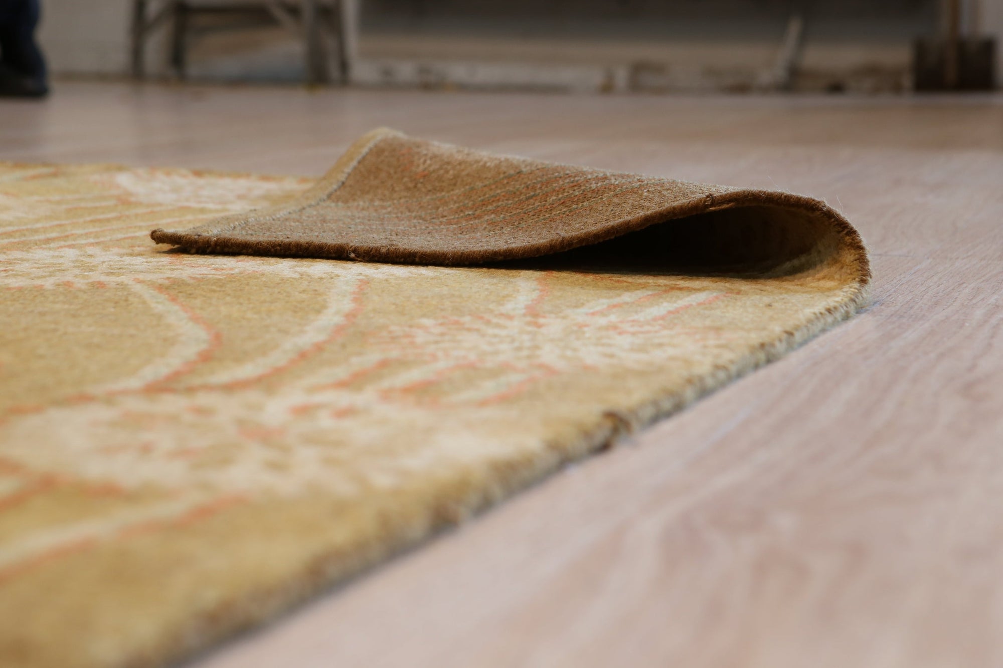 Lila Jasmine Brown Hand Knotted Wool Rug, showcasing its intricate hand-knotted construction and warm brown hues, partially visible in a softly lit room setting.