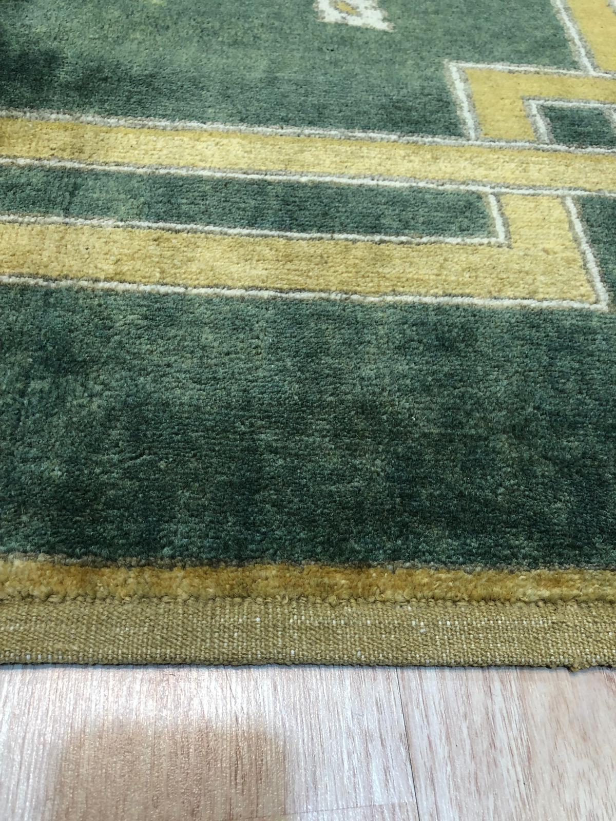 Sloane Louie Green Hand Knotted Wool Rug, its muted greens and subtle pattern complementing a modern living room with a light wood coffee table and beige sofa.