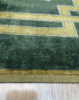 Sloane Louie Green Hand Knotted Wool Rug, its muted greens and subtle pattern complementing a modern living room with a light wood coffee table and beige sofa.