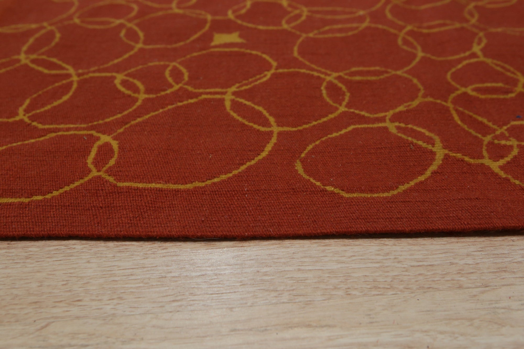 Nadia Lydia Red Flatweave Wool Rug, vibrant red flatweave wool rug partially visible beneath a light wood table leg and woven basket, suggesting a warm, inviting living space.