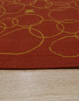 Nadia Lydia Red Flatweave Wool Rug, vibrant red flatweave wool rug partially visible beneath a light wood table leg and woven basket, suggesting a warm, inviting living space.