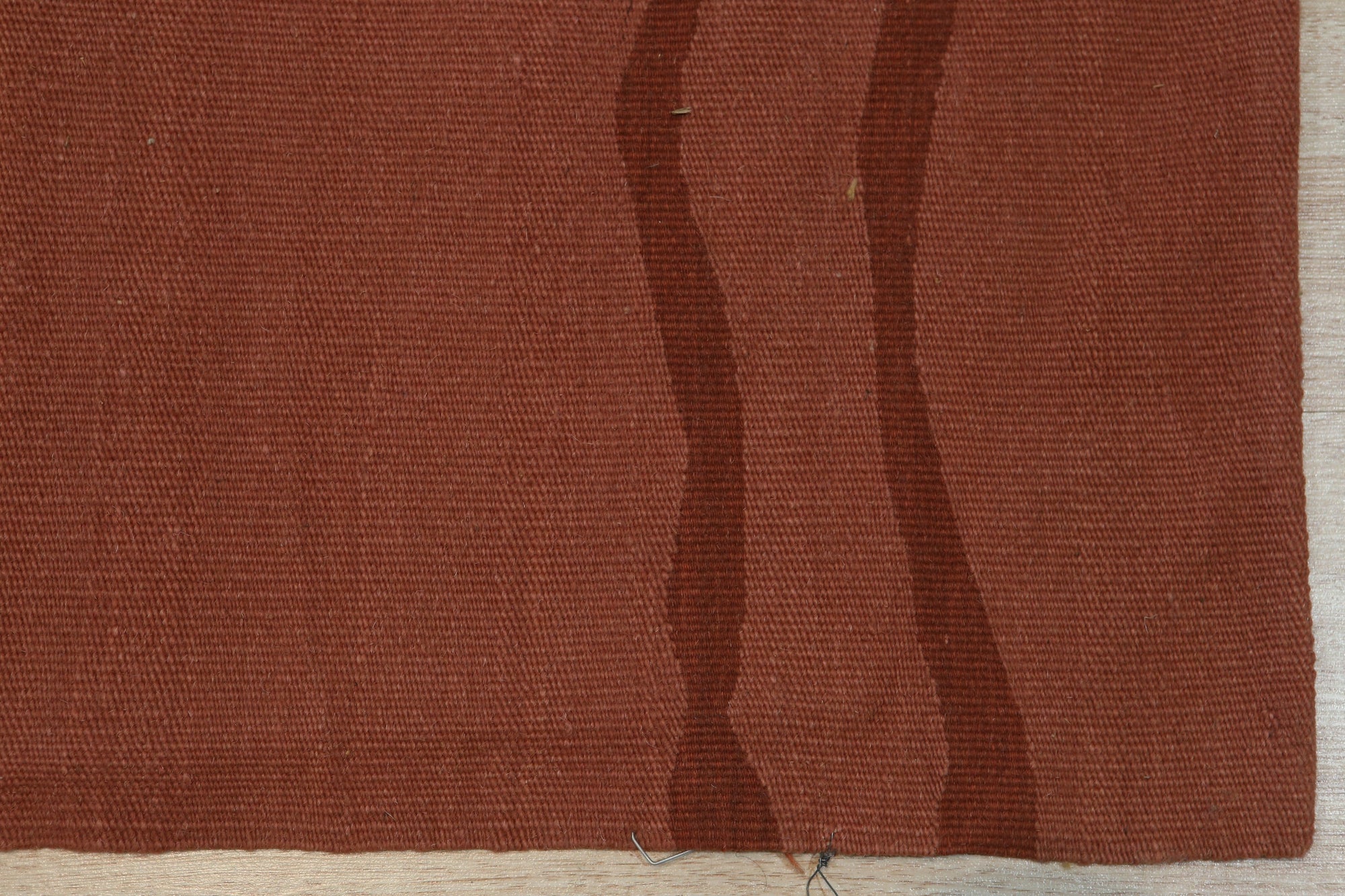 Inviting Maya Rust Flatweave Wool Rug, a warm rust-toned wool rug with a subtle geometric flatweave pattern, partially visible under a modern coffee table in a bright living space.