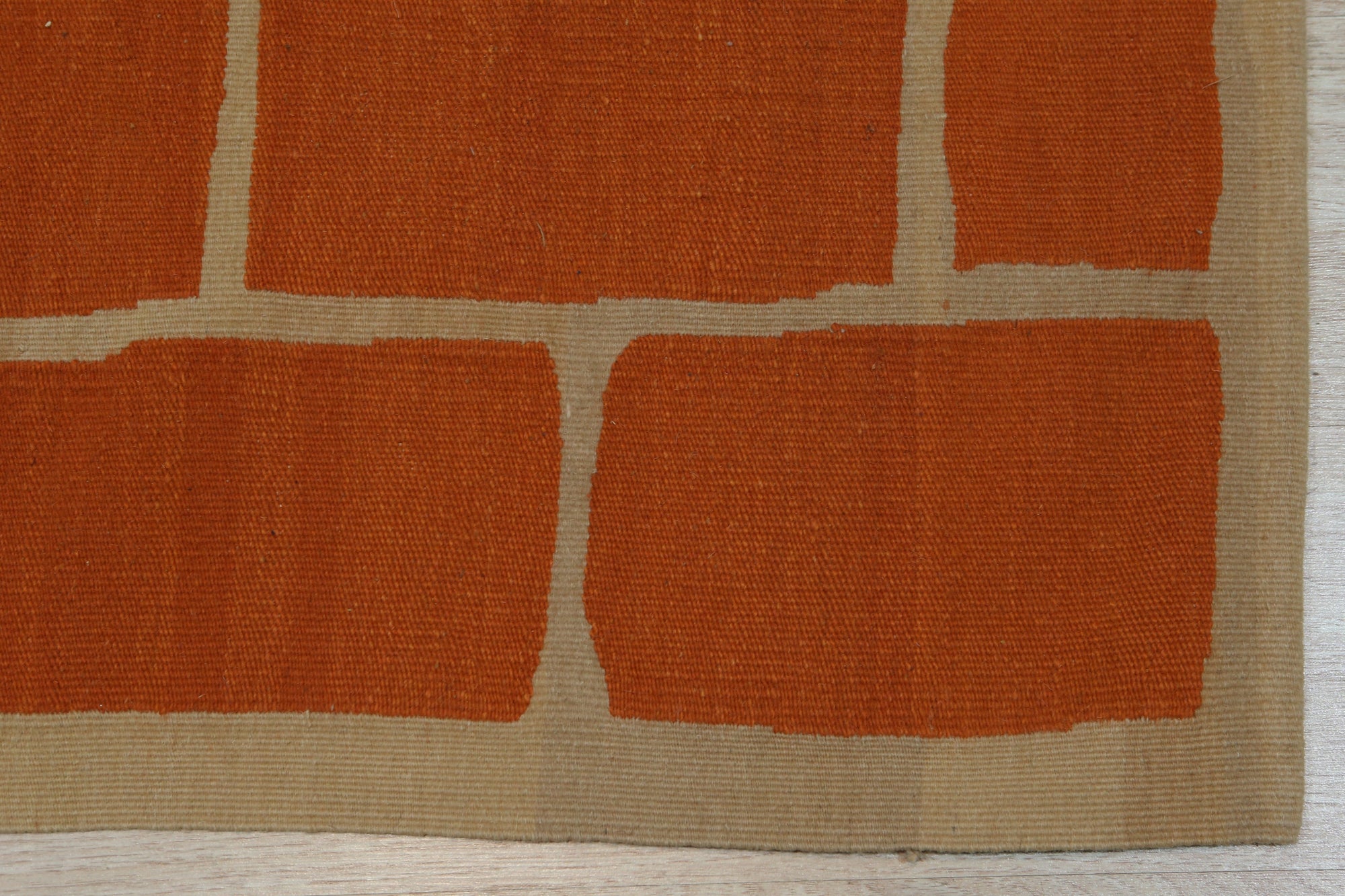 Kira Amara Orange Flatweave Wool Rug, vibrant orange and cream geometric pattern flatweave, lies gracefully on a light wooden floor, adding warmth and modern style to the room.