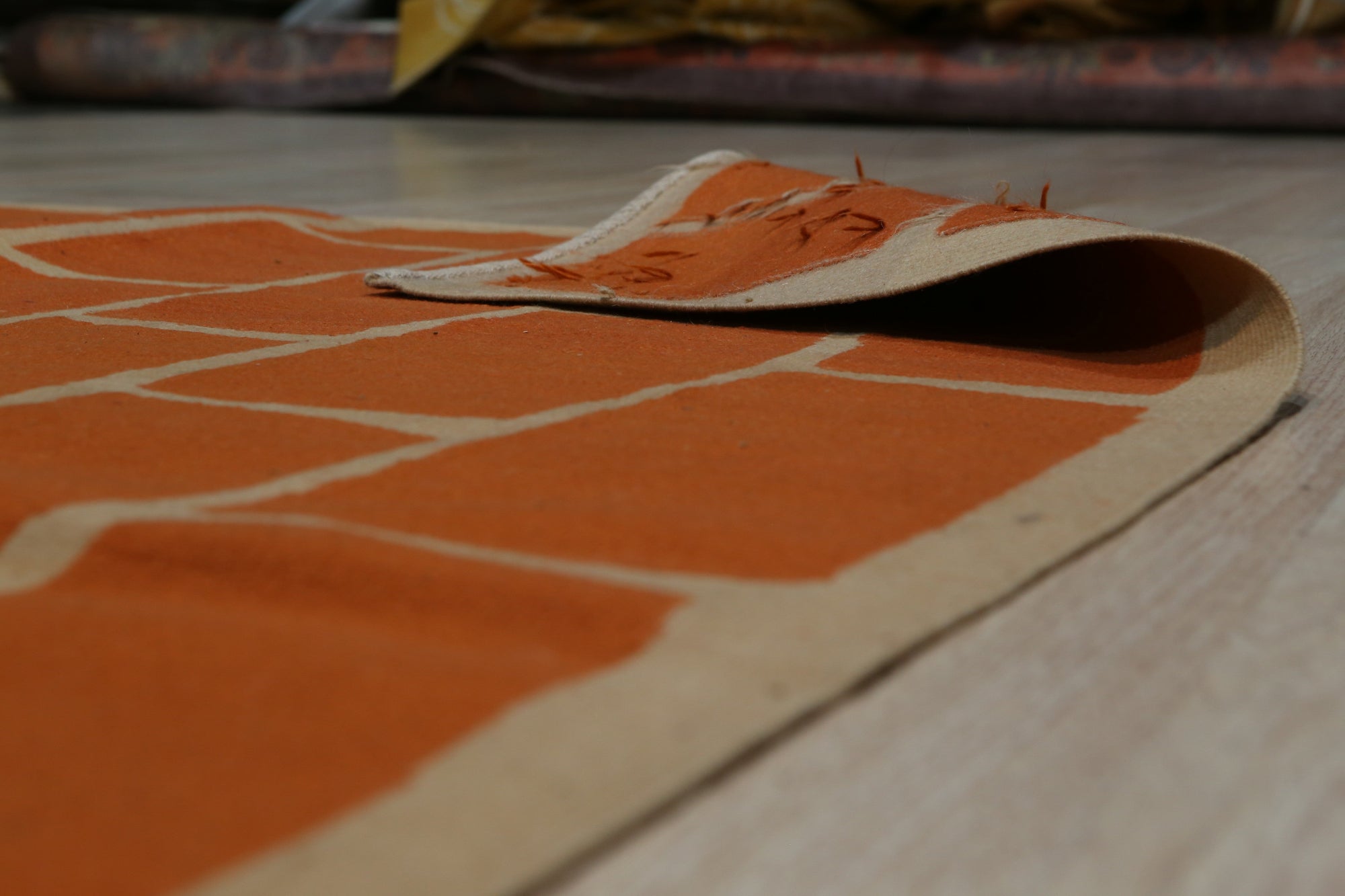 Kira Amara Orange Flatweave Wool Rug, showcasing a vibrant orange and cream geometric pattern in a modern living room setting. Light wood floors and a neutral sofa complement the rug's warm tones.