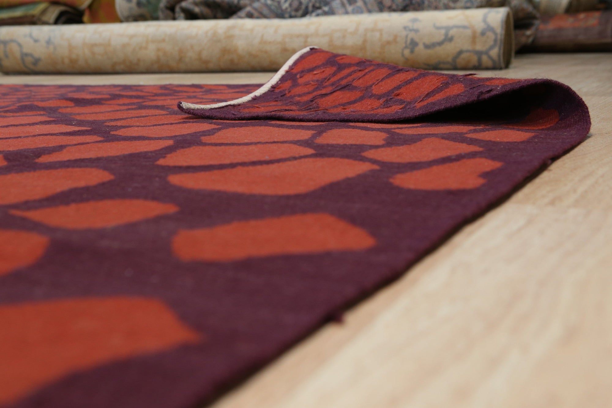 Ella Mira Orange Flatweave Wool Rug, a warm, textured wool rug with a geometric pattern in shades of orange, cream, and grey, displayed on a light hardwood floor.