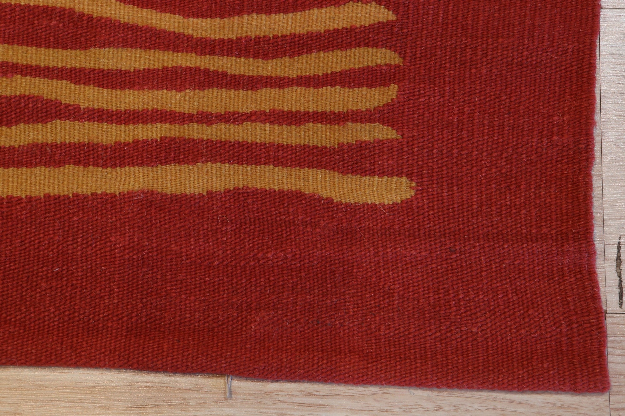 Trendy Sloane Red Flatweave Wool Rug, showcasing a vibrant geometric pattern in shades of red, cream, and gray, lies flat on a hardwood floor, its tight wool weave adding warmth and texture to a bright, modern living space.