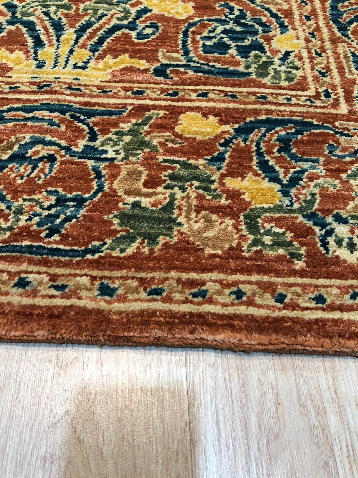 Elegant Warm Red Hand Knotted Wool Rug, its intricate floral patterns unfolding across a rich, warm red wool field, seen in a bright living space, suggesting comfort and timeless elegance.