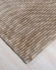 Sloane Freya Brown Hand Tufted Wool Rug, a warm brown and cream rug with a subtle geometric pattern, lies elegantly on a light hardwood floor, partially beneath a dark wood coffee table, showcasing its plush texture and grounding presence in a living space.
