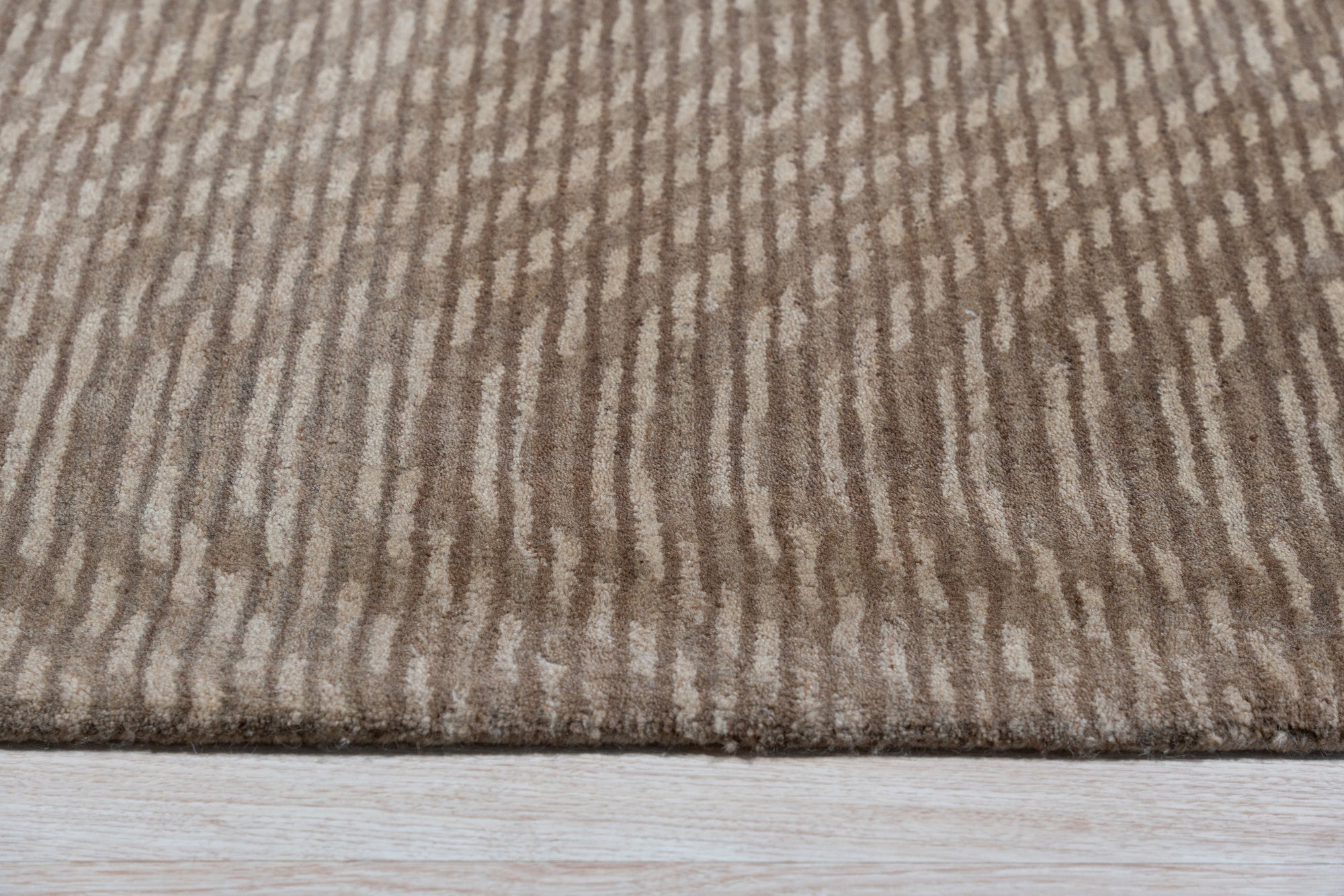 Sloane Freya Brown Hand Tufted Wool Rug, nestled on a light wood floor, features a textured geometric pattern in varying shades of brown, cream, and beige, creating a warm and inviting atmosphere.