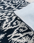 Luna Willow Black, White Hand Tufted Wool Rug, with its graphic black and white pattern, anchors a modern living room with light wood floors and minimalist furniture, showcasing its bold geometric design.