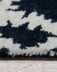 Luna Willow Black, White Hand Tufted Wool Rug sprawls across a warmly lit living room, its geometric black and white pattern anchoring a contemporary space with natural wood floors and minimal furnishings.
