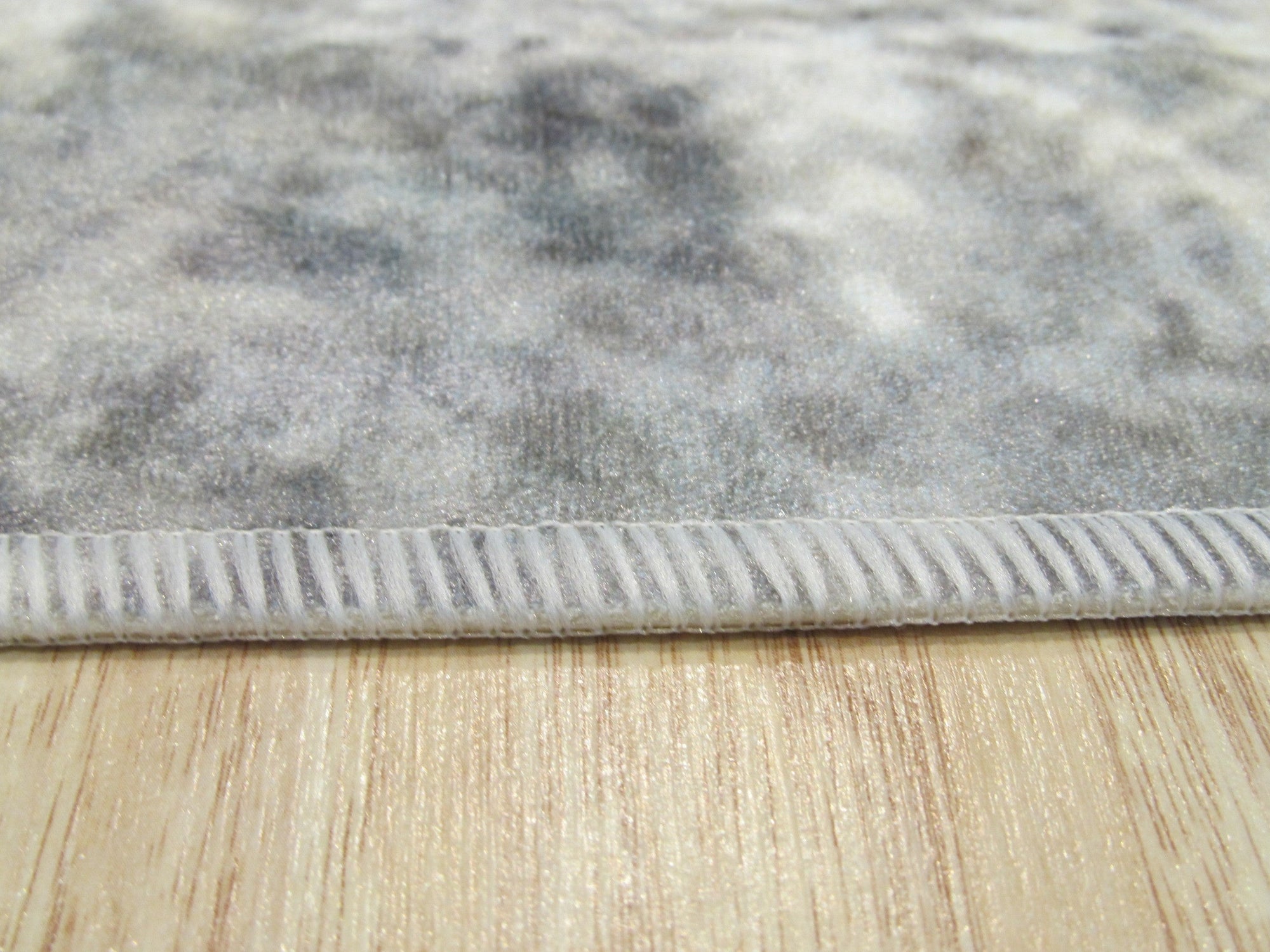 Bianca Warm Gray Machine Made Rug displayed, revealing subtle texture and warm grey tones against a light wood floor and white furniture, suggesting a contemporary living space.