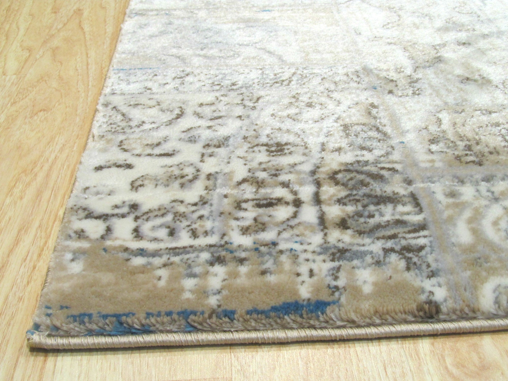 Sarrah Trara Ivory Machine Made Rug displayed in a bright, modern living room. The ivory-colored rug anchors the space, its subtle, patterned design complementing light wood flooring and neutral furniture.