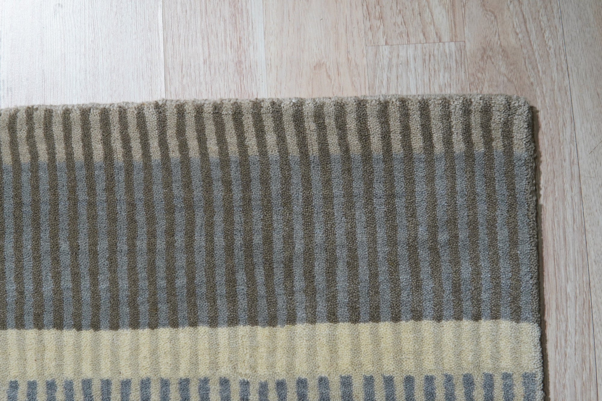 Zinnia Striped Green Handmade Wool Rug graces a sun-drenched hardwood floor, its vibrant green and cream stripes radiating warmth and texture in a modern living space.