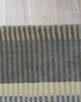 Zinnia Striped Green Handmade Wool Rug graces a sun-drenched hardwood floor, its vibrant green and cream stripes radiating warmth and texture in a modern living space.