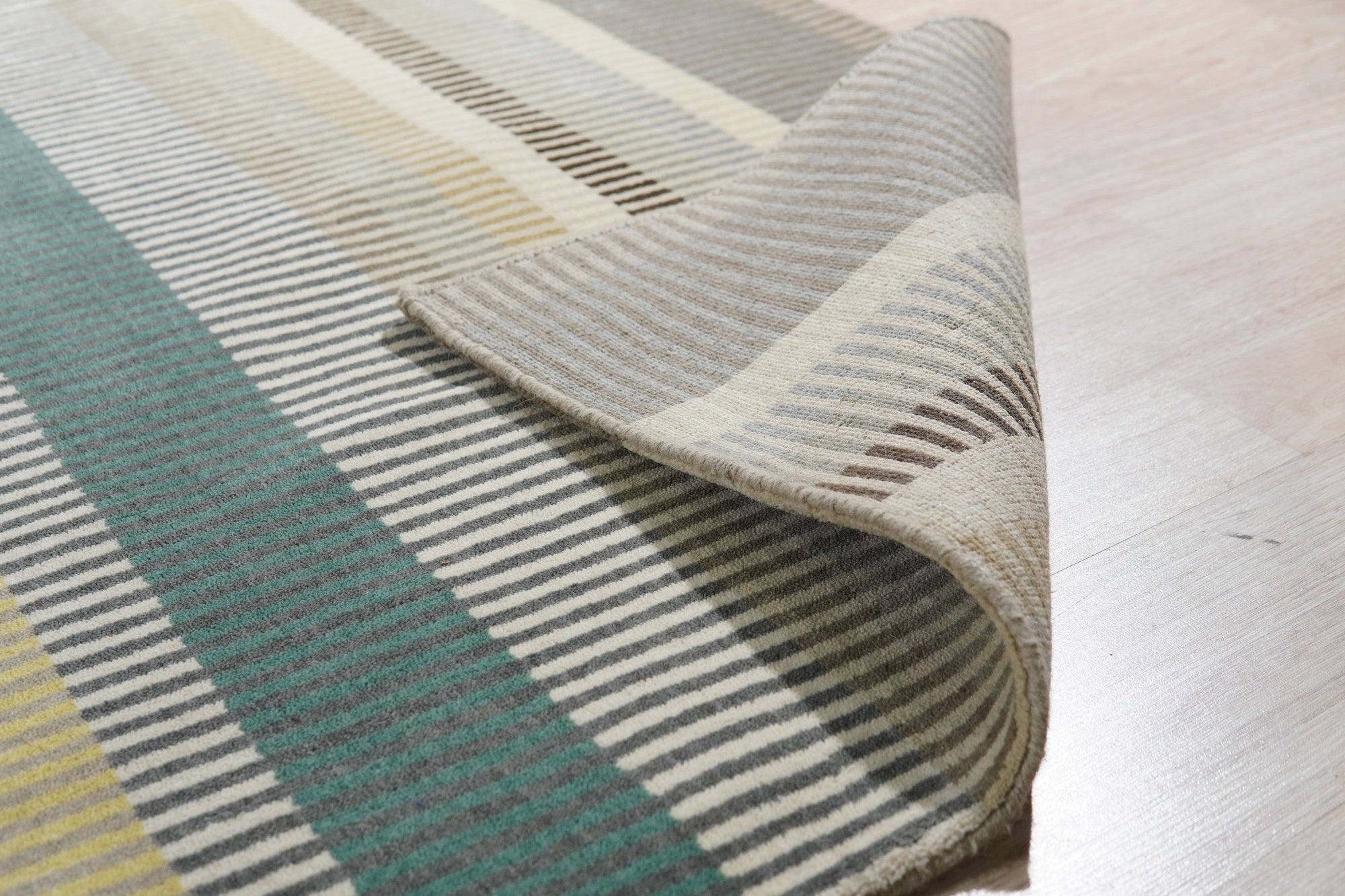 Zinnia Striped Green Handmade Wool Rug displayed in a bright, airy living space. Natural light highlights the rug's vibrant green and neutral stripes, showcasing its textured wool construction and handmade quality. The rug anchors a contemporary seating area, lending a fresh, organic feel to the room.