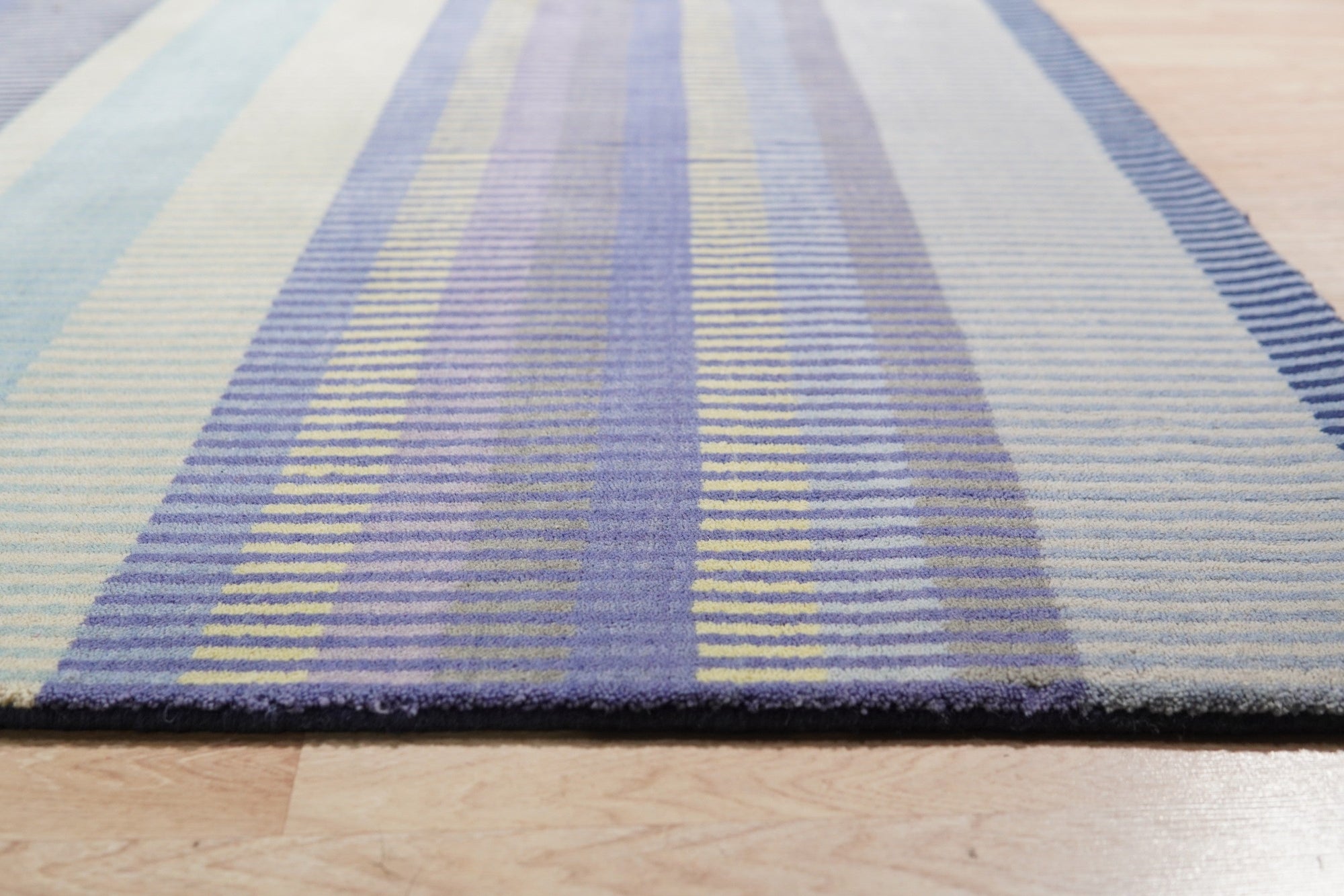 Comfortable Striped Lavender Handmade Wool Rug, its soft lavender and cream stripes creating a soothing texture underfoot, lies on a hardwood floor in a sunlit room.