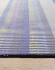 Comfortable Striped Lavender Handmade Wool Rug, its soft lavender and cream stripes creating a soothing texture underfoot, lies on a hardwood floor in a sunlit room.