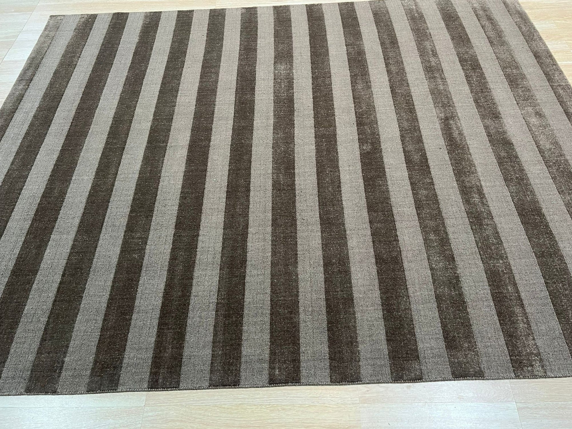 Yara Alluring Brown Handmade Wool Rug, featuring warm brown tones and a subtle, textured design, laying elegantly on a hardwood floor with natural light highlighting its wool construction.