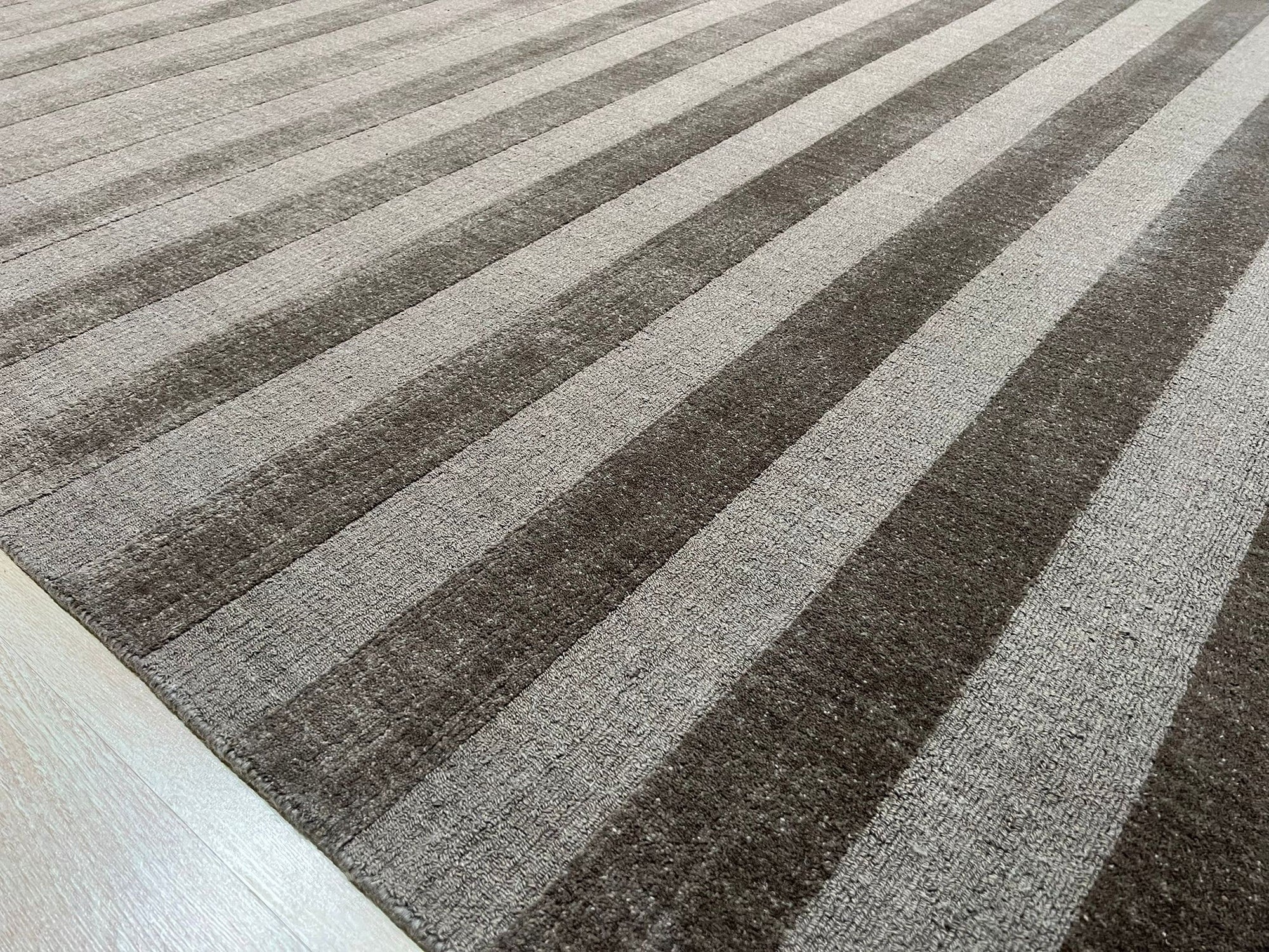 Yara Alluring Brown Handmade Wool Rug, showcasing its intricate geometric pattern and warm brown tones, layered over a dark hardwood floor in a modern living room setting. The rug's texture adds depth and comfort to the space.