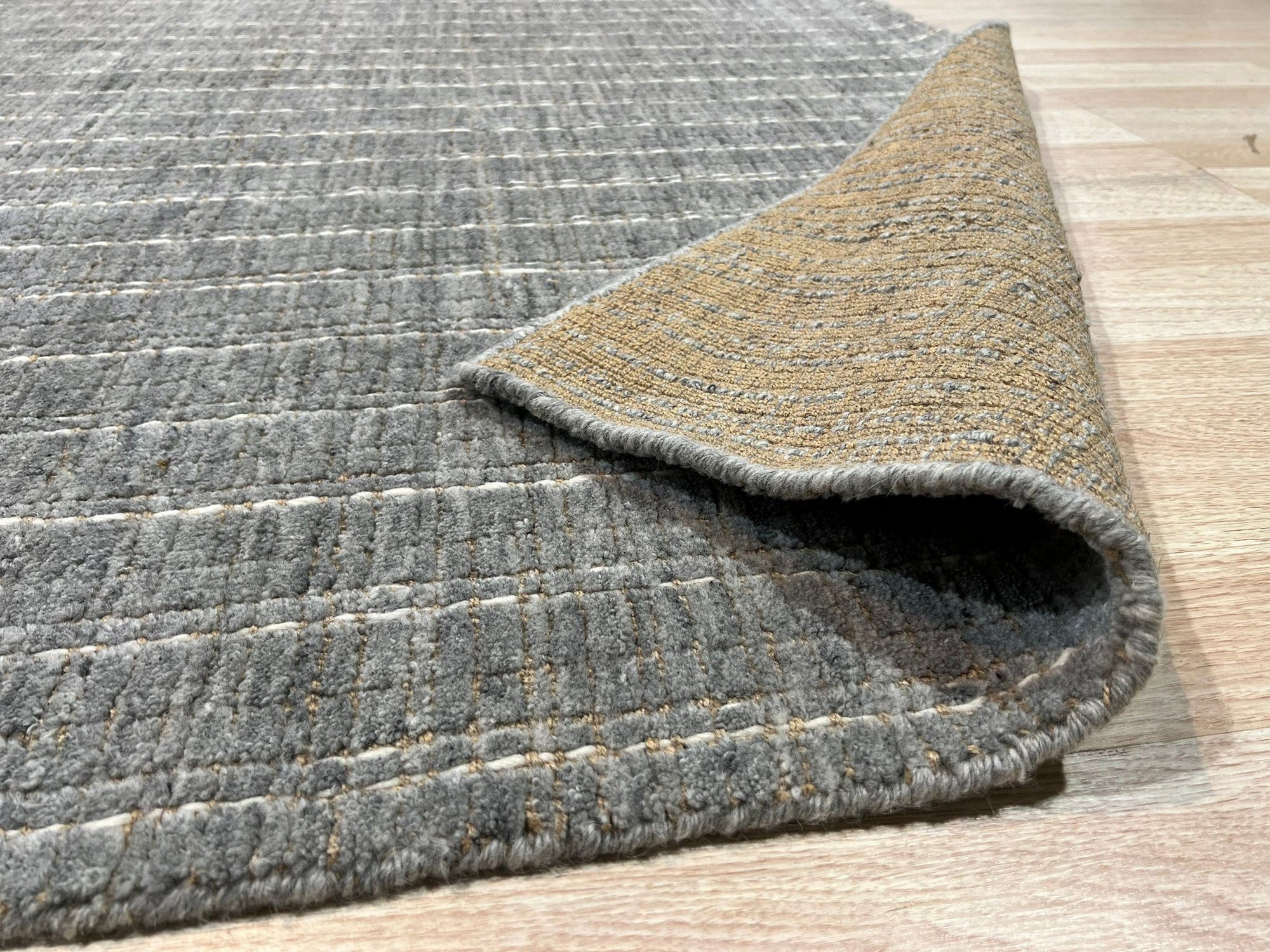 Delicate Giselle Gray Handmade Wool Rug, displaying subtle gray variations and intricate detailing, resting on a light wood floor in a bright, modern interior.