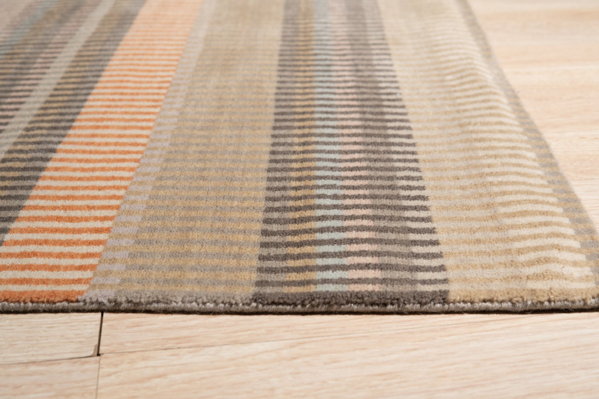 Louie Ophelia Beige Handmade Wool Rug, exhibiting a subtle, elegant pattern in soft beige tones, lays flat against a light floor, showcasing its texture and overall design within a room setting.