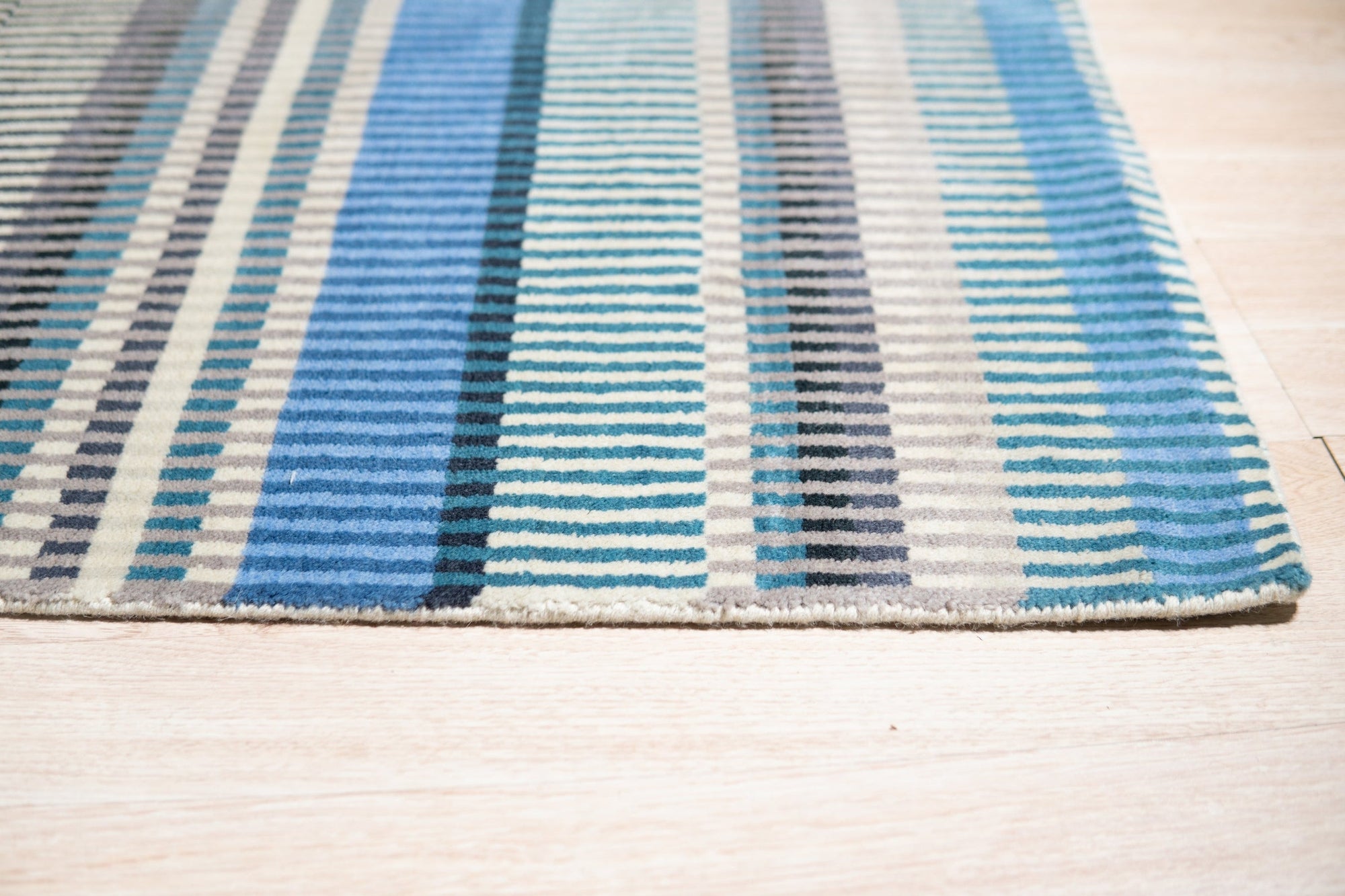 Louie Ophelia Ocean Blue Handmade Wool Rug, its intricate pattern unfolding in shades of ocean blue and cream, lays gracefully on a polished hardwood floor, hints of sunlight highlighting the rug's soft wool texture.