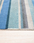 Louie Ophelia Ocean Blue Handmade Wool Rug, its intricate pattern unfolding in shades of ocean blue and cream, lays gracefully on a polished hardwood floor, hints of sunlight highlighting the rug's soft wool texture.