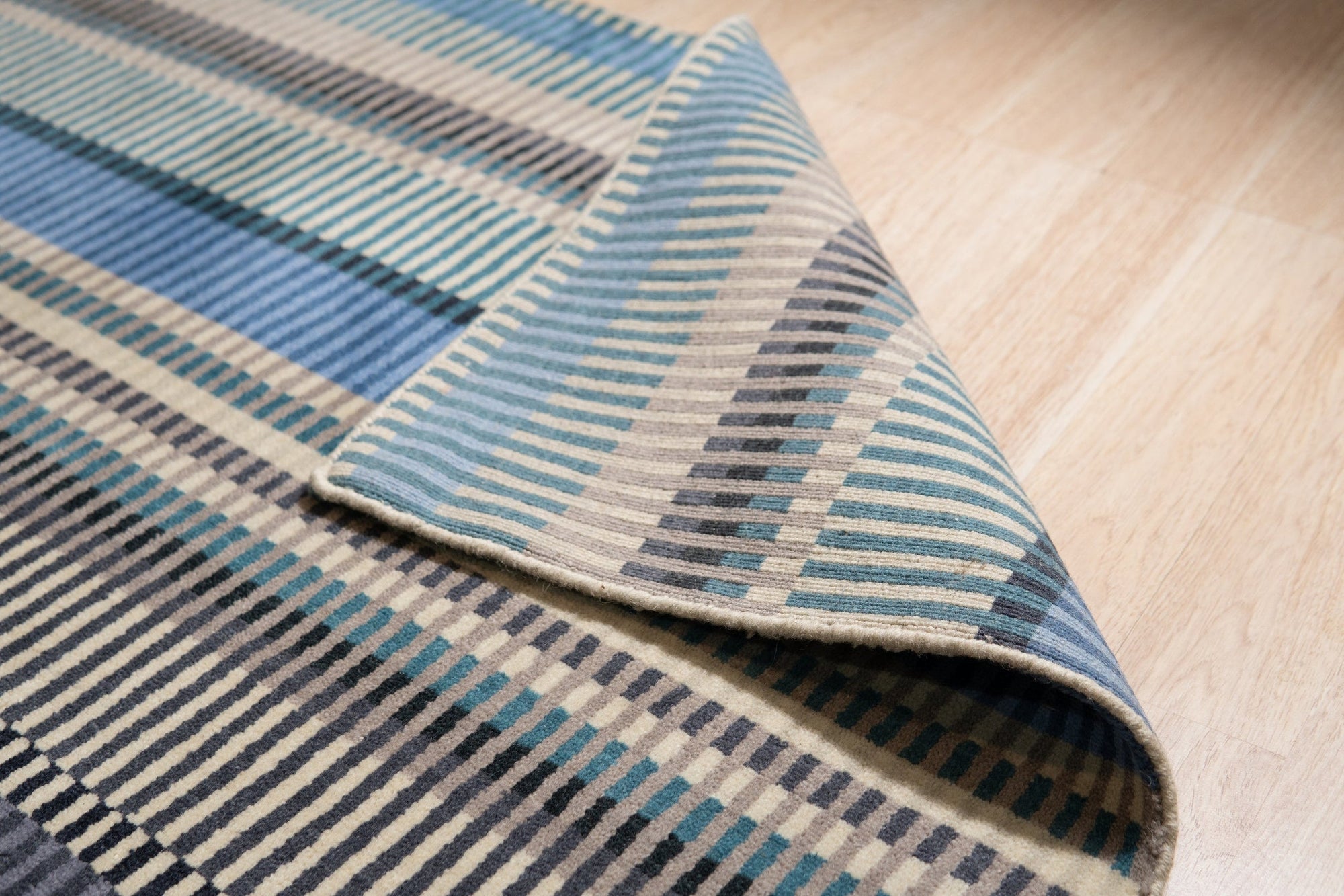 Louie Ophelia Ocean Blue Handmade Wool Rug, presenting a swirling, watery design in shades of blue, cream, and hints of brown, laid flat showcasing its intricate hand-knotted construction.