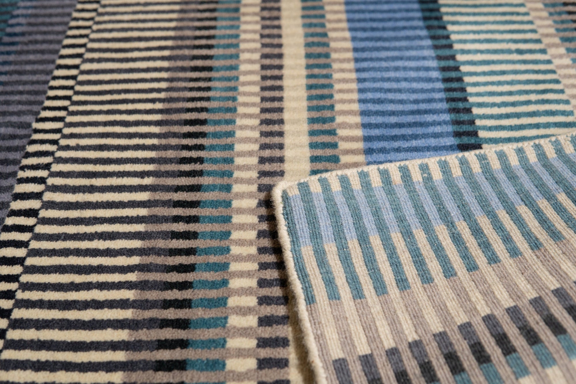 Louie Ophelia Ocean Blue Handmade Wool Rug, its intricate design radiating a sense of calm, lays on a light wooden floor, warmed by soft natural light, showcasing the rug's subtle texture and vibrant ocean blue hues.