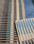 Louie Ophelia Ocean Blue Handmade Wool Rug, its intricate design radiating a sense of calm, lays on a light wooden floor, warmed by soft natural light, showcasing the rug's subtle texture and vibrant ocean blue hues.