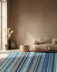 Louie Ophelia Ocean Blue Handmade Wool Rug displayed on a light wood floor, its intricate pattern and varying shades of blue creating a soothing ocean-inspired ambiance in a room setting.
