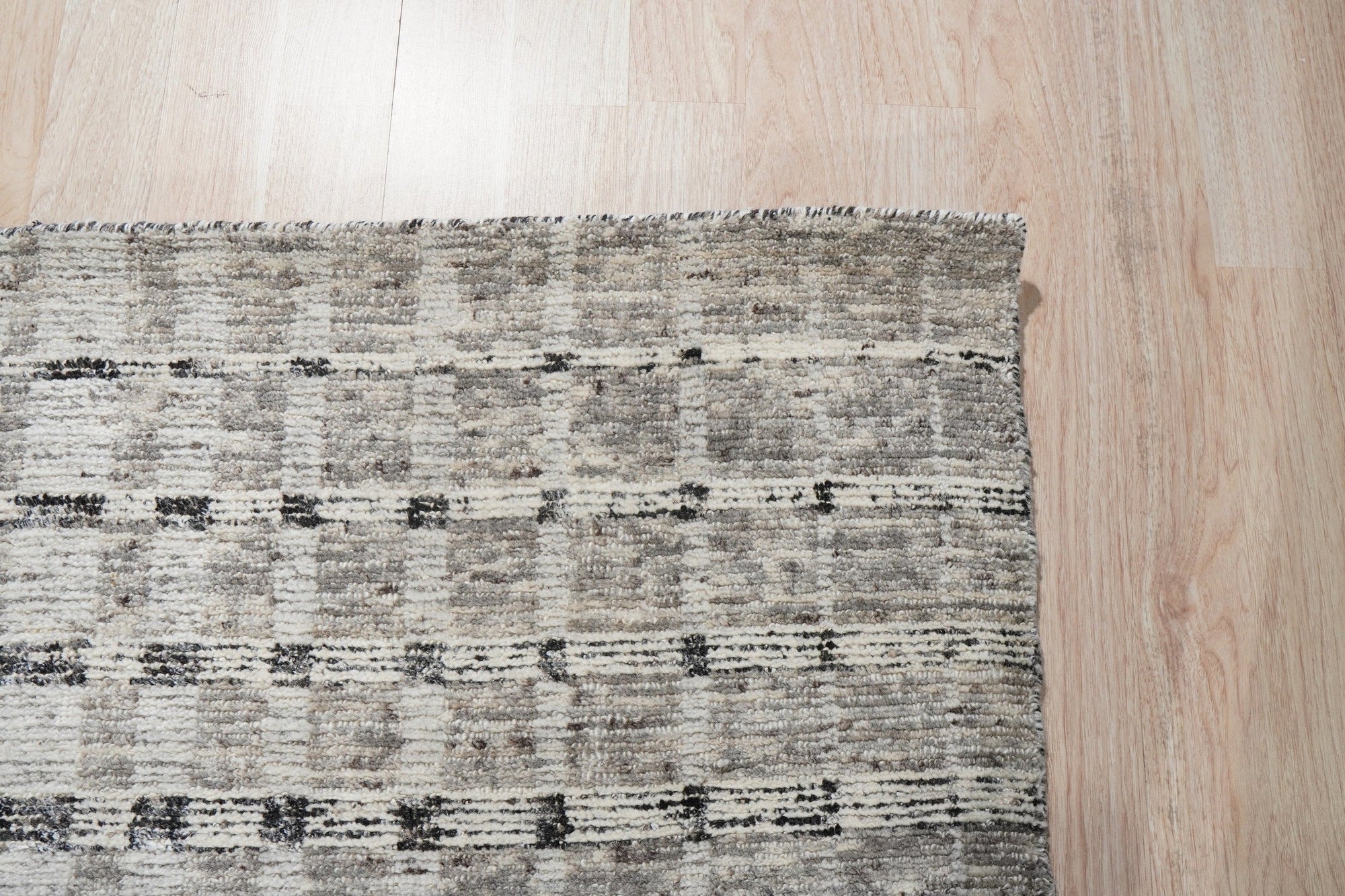 Nadia Ava Gray Handmade Wool Rug, soft gray wool rug with subtle pattern variations, displayed in a bright, minimalist living room setting with light wood floors and modern furniture.
