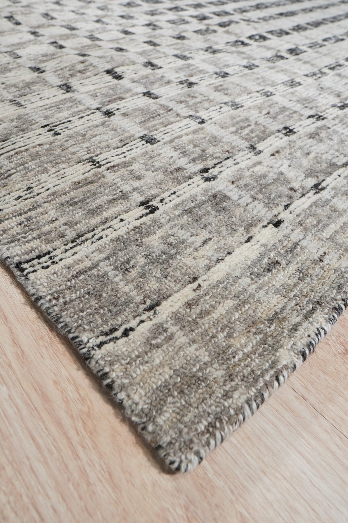 Nadia Ava Gray Handmade Wool Rug in a warmly lit living room, blending seamlessly with neutral furniture and hardwood floors. Gray tones in the rug create subtle patterns, providing a grounding element in the modern interior.