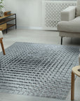 Nadia Ava Gray Handmade Wool Rug, softening a bright, modern living room. Neutral hues and subtle texture of the wool rug ground a space with white walls, a minimalist sofa, and natural light pouring through a window.
