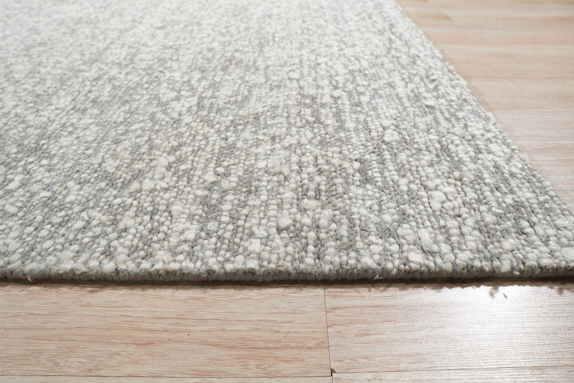 Opulent Alluring Silver Handmade Wool Rug, its silvery sheen radiating across a polished floor, showcasing intricate hand-knotted detailing and the luxurious texture of wool.