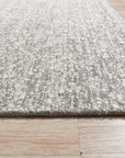 Opulent Alluring Silver Handmade Wool Rug, its silvery sheen radiating across a polished floor, showcasing intricate hand-knotted detailing and the luxurious texture of wool.
