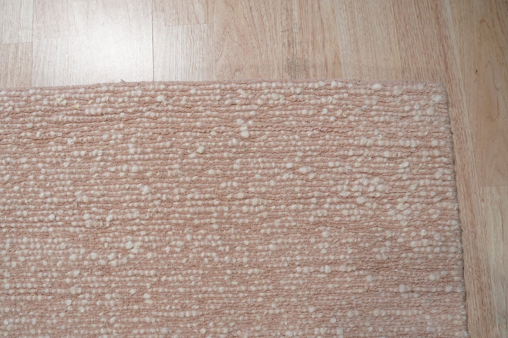 Freya Graceful Pink Handmade Wool Rug, showcasing its soft pink hues and plush wool texture, rests elegantly on a light hardwood floor, its subtle pattern adding warmth and a touch of handcrafted luxury to the room.