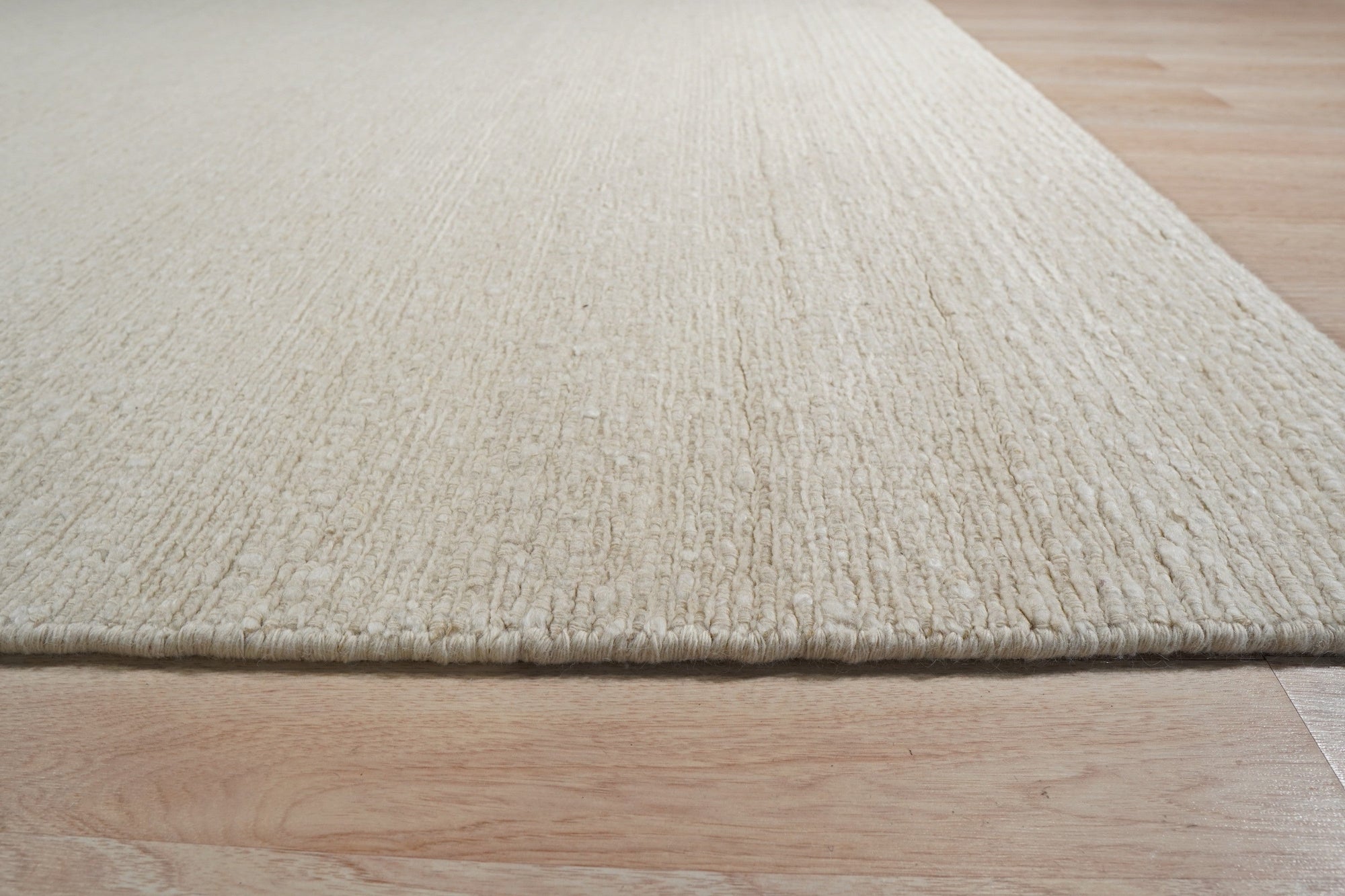 Bespoke Delicate Ivory Handmade Wool Rug, softly textured and ivory-toned, lies flat on a light surface. Subtle variations in the wool weave hint at its handcrafted construction, creating a warm and inviting feel.