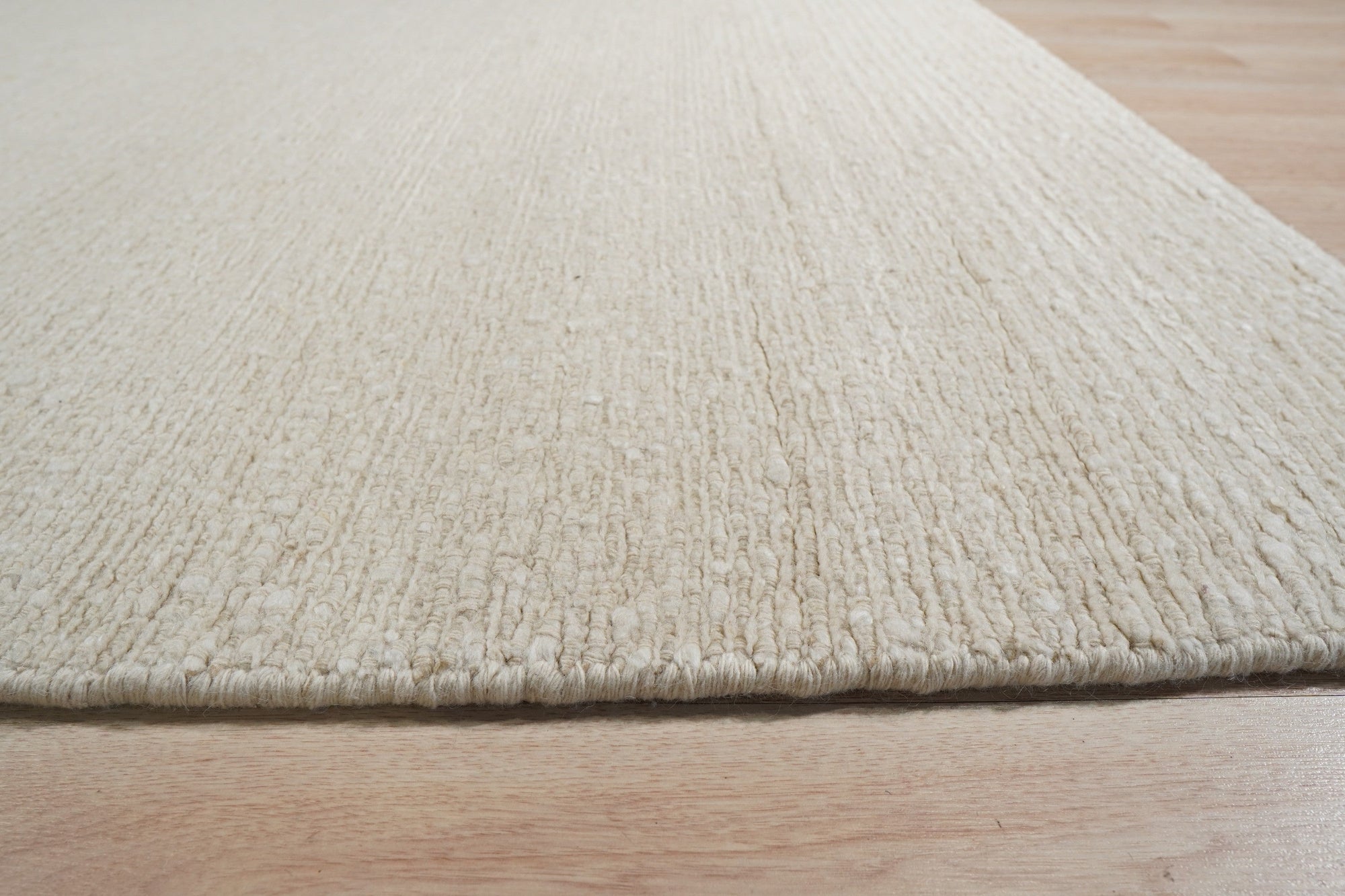 Bespoke Delicate Ivory Handmade Wool Rug, its creamy texture and subtle pattern softening a room bathed in warm, natural light. Hand-knotted wool construction evident in the luxurious pile, its ivory hue bringing serene elegance to the space.