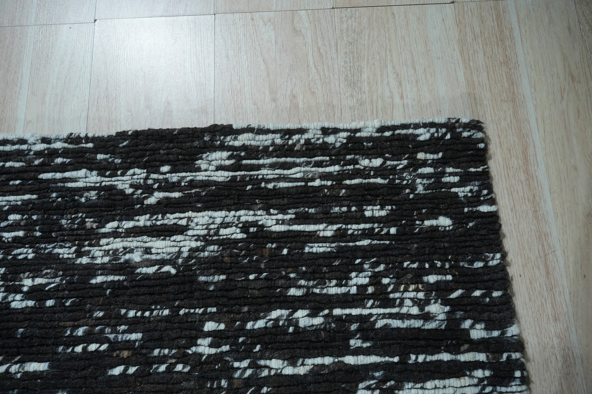Fiona Rustic Black Flatweave Wool Rug, textured black wool flatweave adds rustic warmth to a neutral-toned living room with a beige sofa and textured throw pillows.