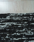 Fiona Rustic Black Flatweave Wool Rug, textured black wool flatweave adds rustic warmth to a neutral-toned living room with a beige sofa and textured throw pillows.