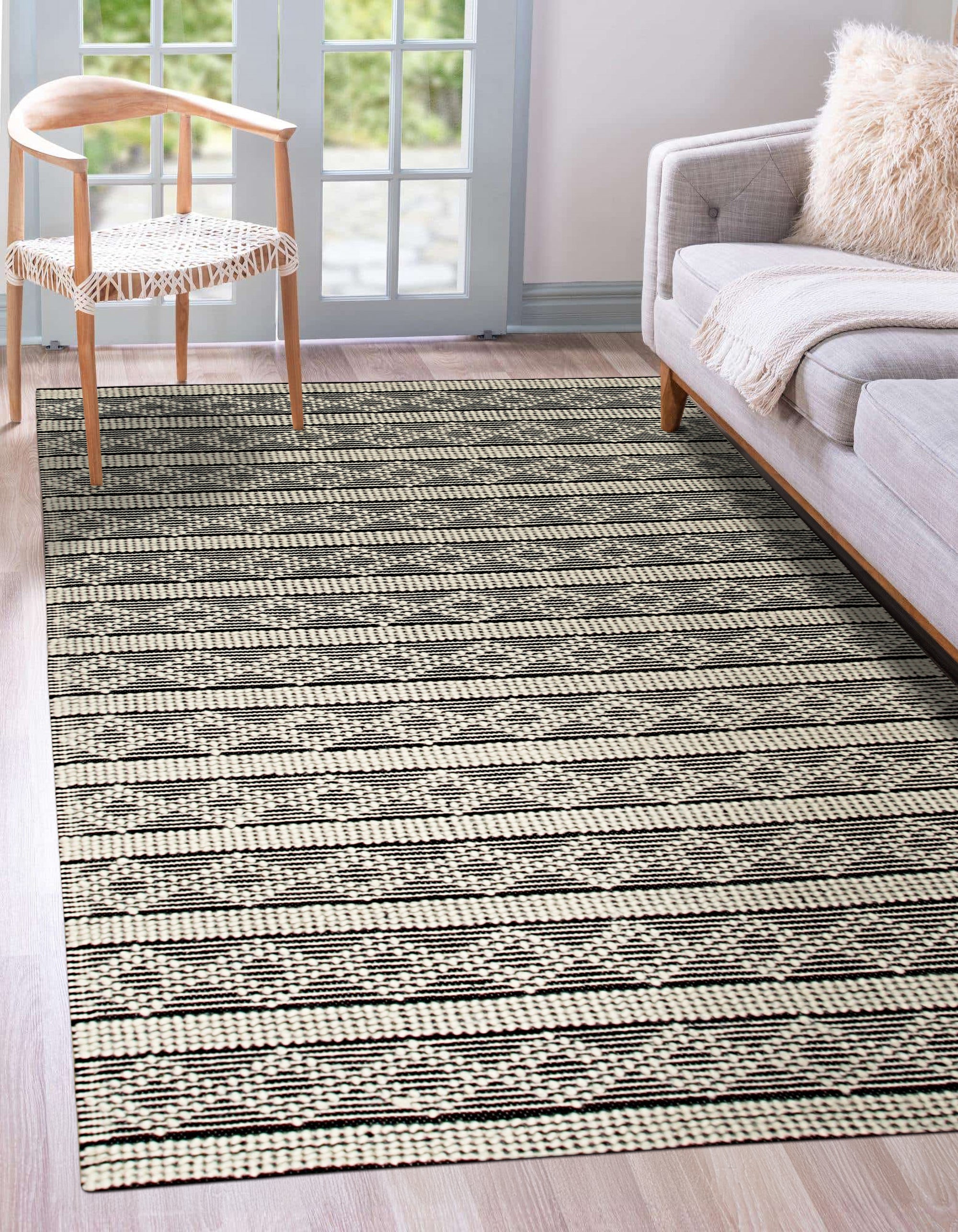 Selene Striped Black Handmade Wool Rug, showcasing bold black and cream stripes in a modern living room setting. Warm wool texture and graphic pattern ground the space, complemented by minimalist furniture.