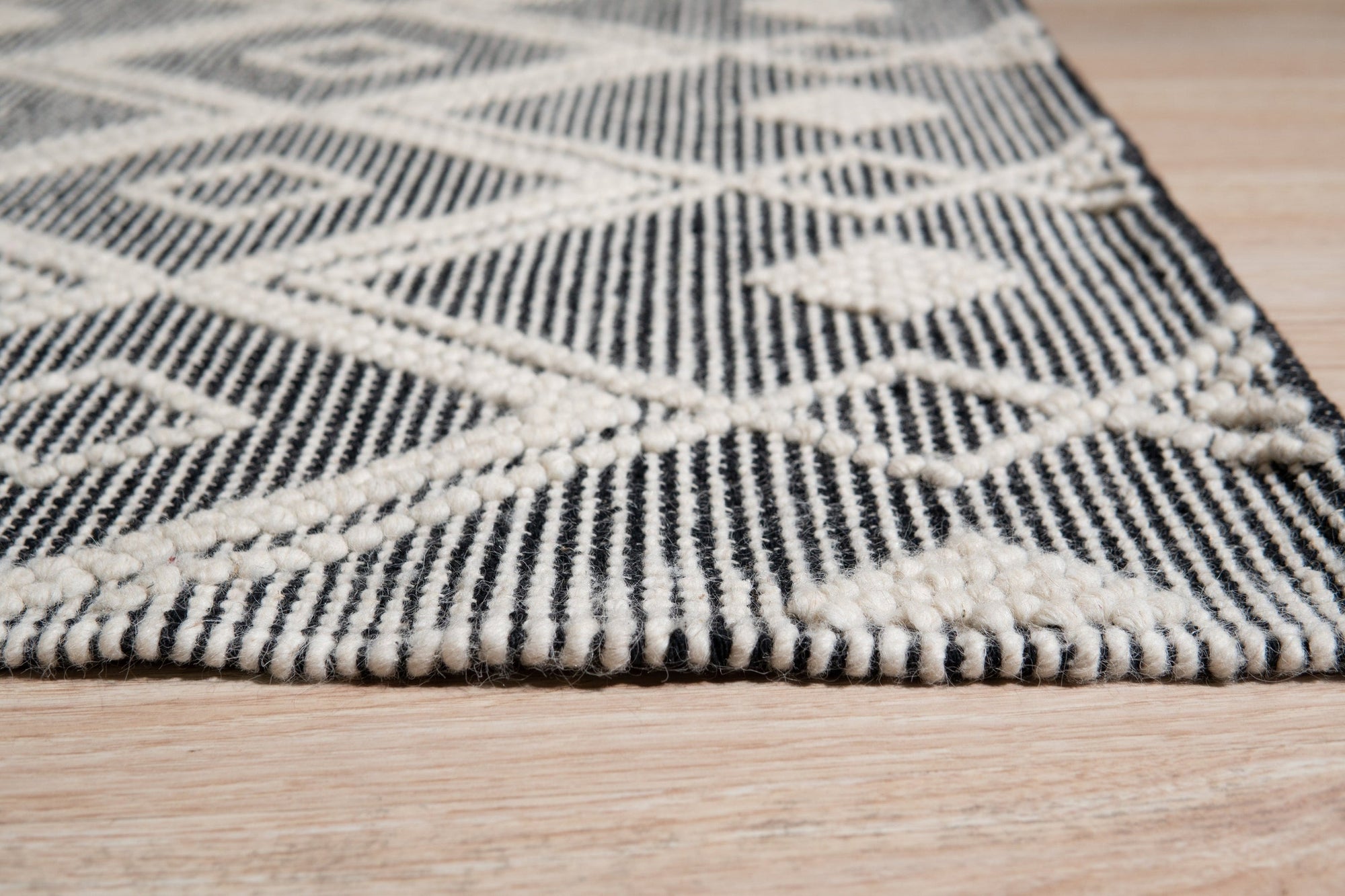 Modern Kilim Black Handmade Wool Rug, showcasing a textured weave with geometric patterns in contrasting black and off-white, lies elegantly on a light hardwood floor, its minimalist design adding sophistication to a modern living space.